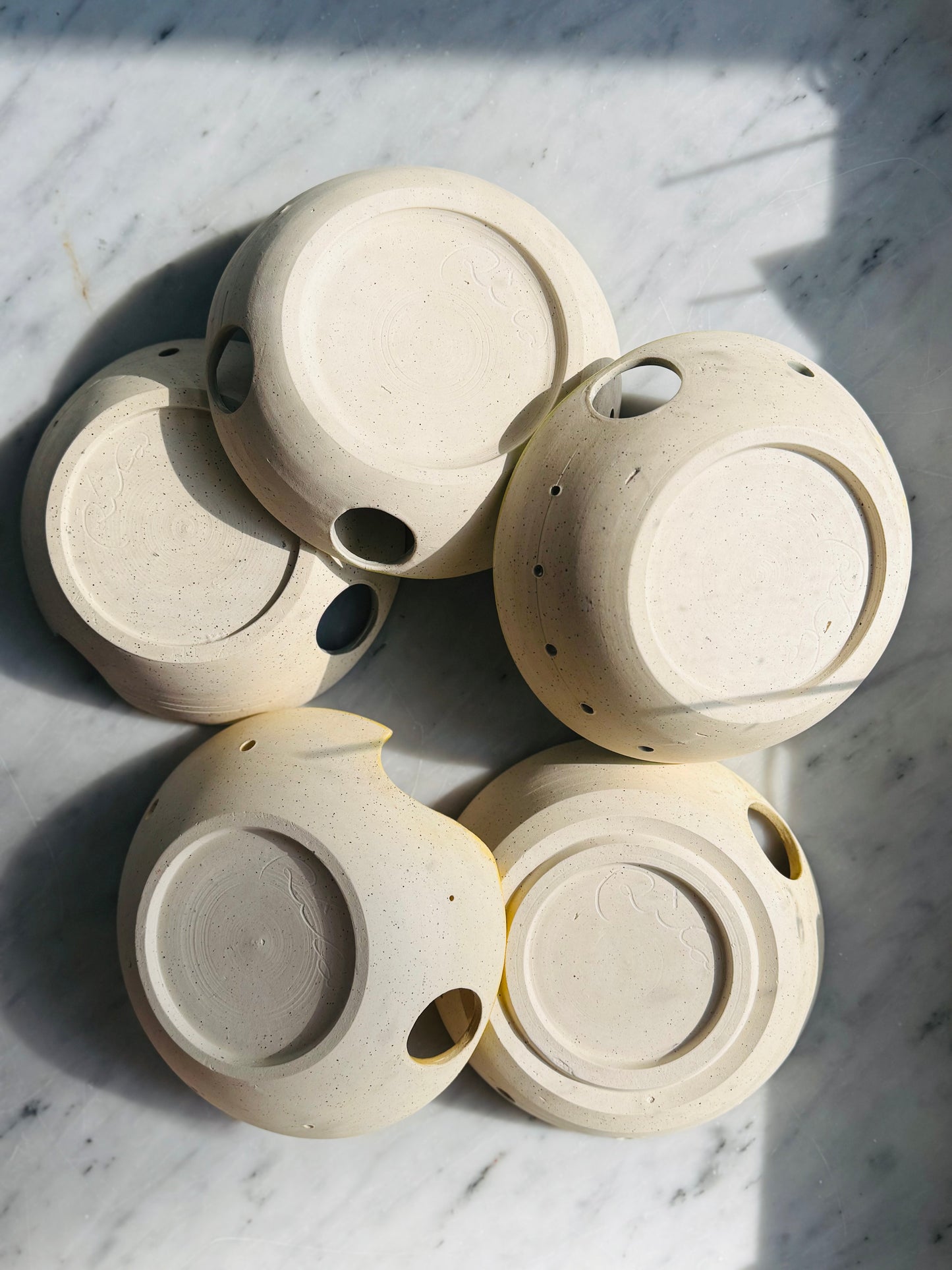 Spread out overhead view of five different Herb stripper with Garlic Grater designs laid upside down by Rita Strayer Ceramics of Savannah. Easily strip leaves from your favorite herb. Made from Stoneware clay. Available in chartreuse (green) or yellow interior bowl colors, with either 1 or 2 thumb holes for ease of use and hanging up when you're done.