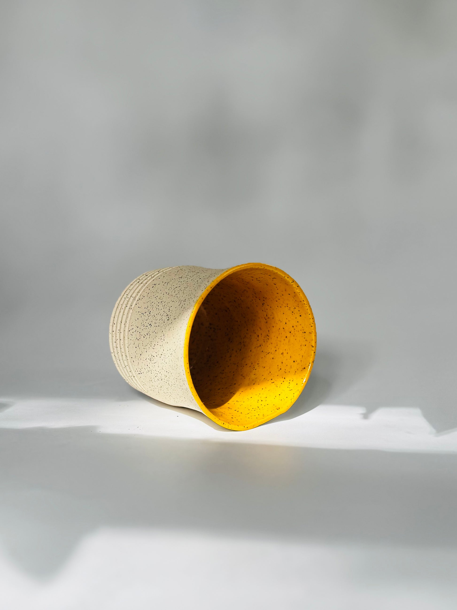 Cylindrical ceramic tumbler made by Rita Strayer Ceramics of Savannah. This 10oz mug has a textured surface and yellow interior on a blackish-grey background.