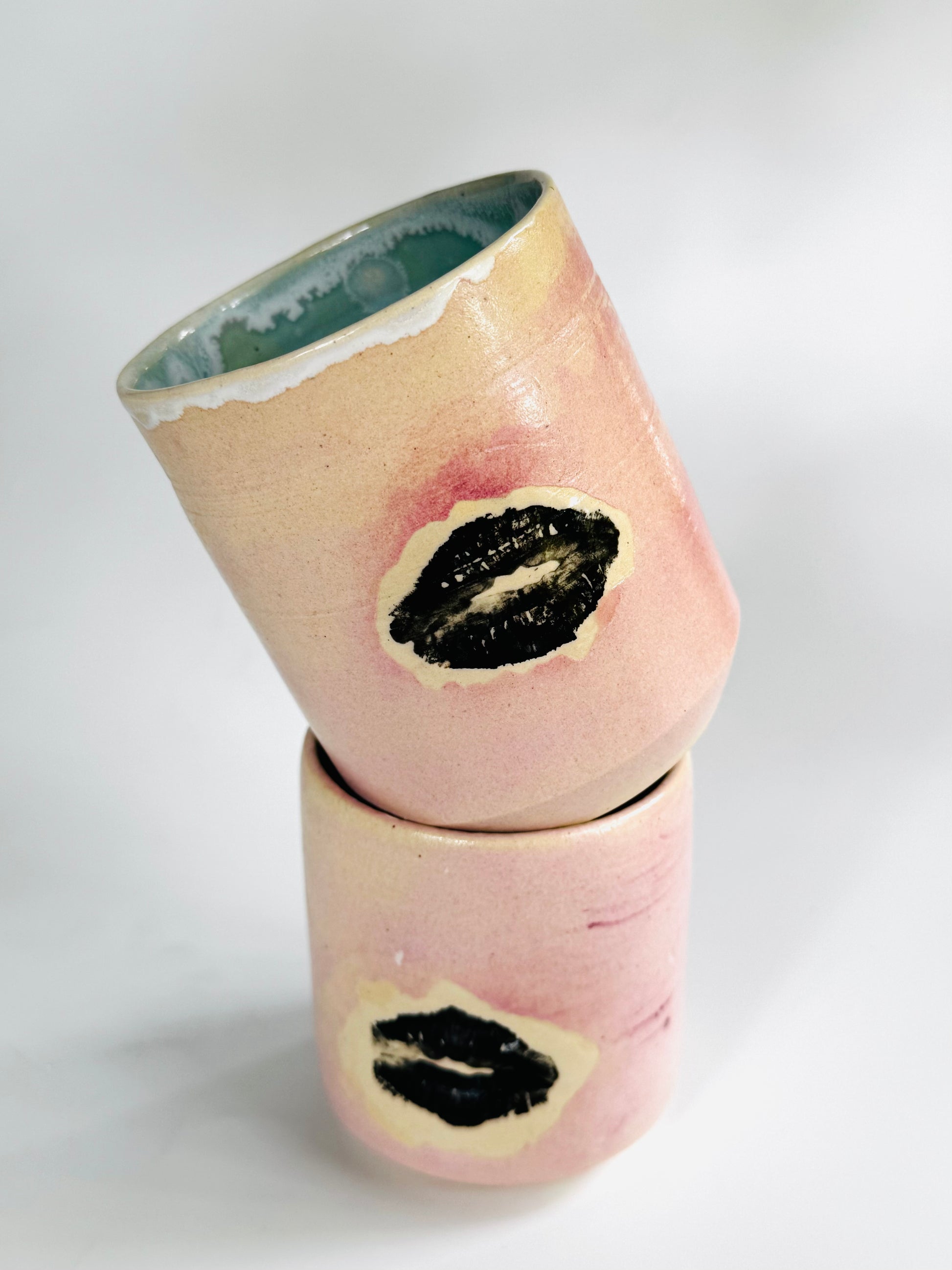 Playful tumbling view of the Large Kissy Cup Tumbler by Rita Strayer Ceramics of Savannah. Cascading flux rim, various sea foam interior and celadon bloom shads. Stoneware, microwavable, black lip design with pink dominant colors.