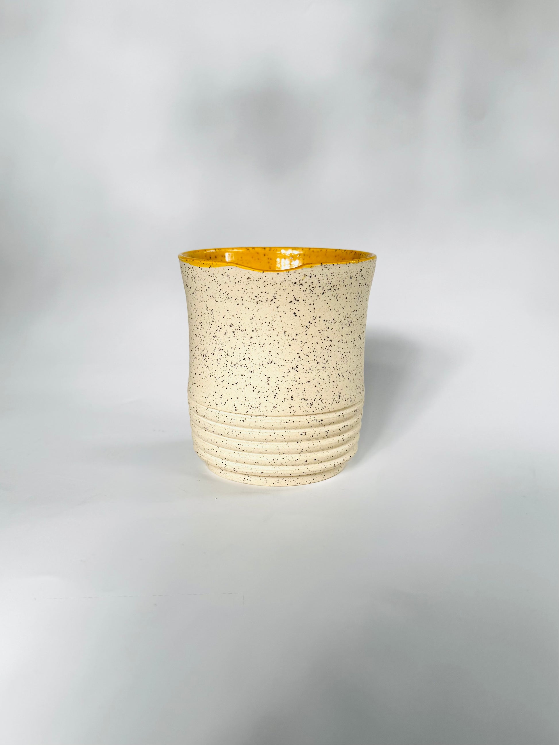 Ceramic cup with textured beige body and yellow interior on a white background. For hot and cold drinks alike. 