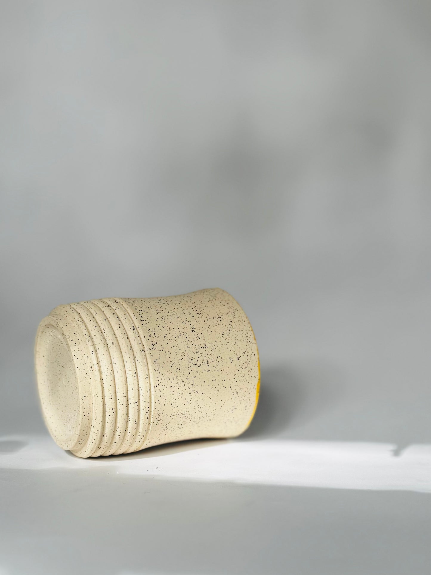 Beige textured cylindrical tumbler mug by Rita Strayer Ceramics of Savannah. Side set shot of a blackish-gray exterior 10oz tumbler.