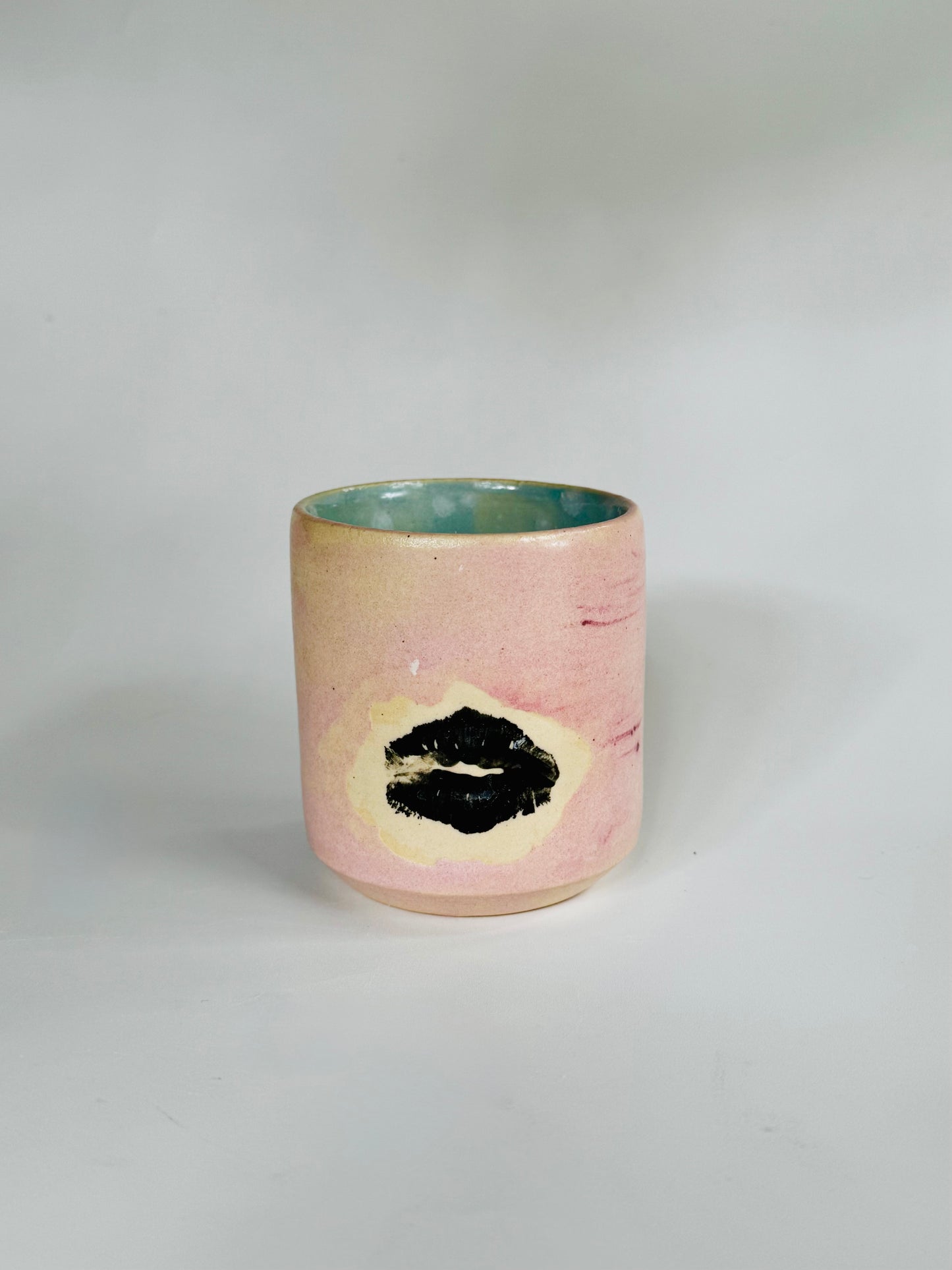 Straight over view of the Small Kissy Cup Tumbler by Rita Strayer Ceramics of Savannah. This design features a cascading flux rim, various sea foam interior and celadon bloom shads. Stoneware, microwavable, black lip design with pink dominant colors.