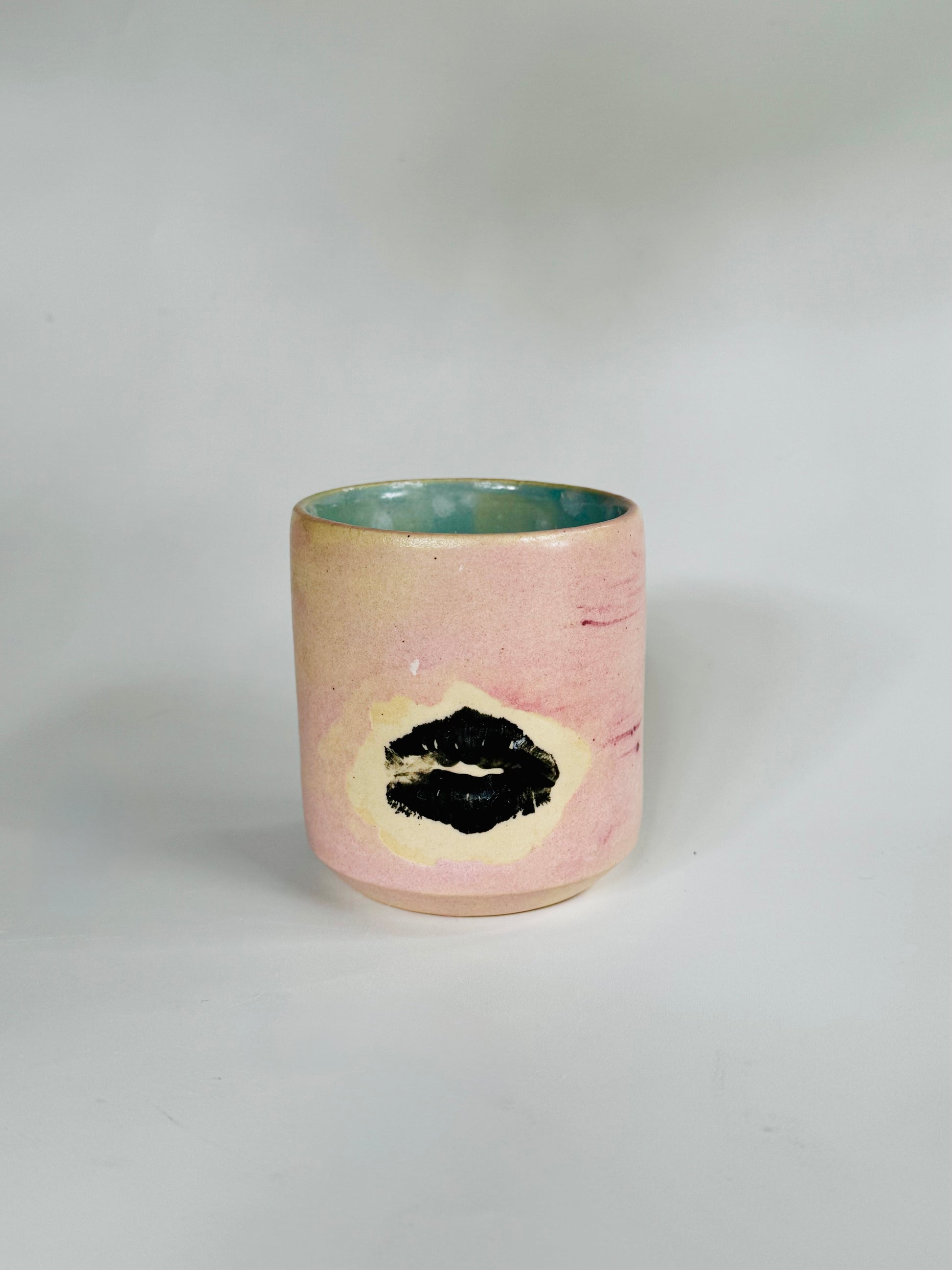 Straight over view of the Small Kissy Cup Tumbler by Rita Strayer Ceramics of Savannah. This design features a cascading flux rim, various sea foam interior and celadon bloom shads. Stoneware, microwavable, black lip design with pink dominant colors.