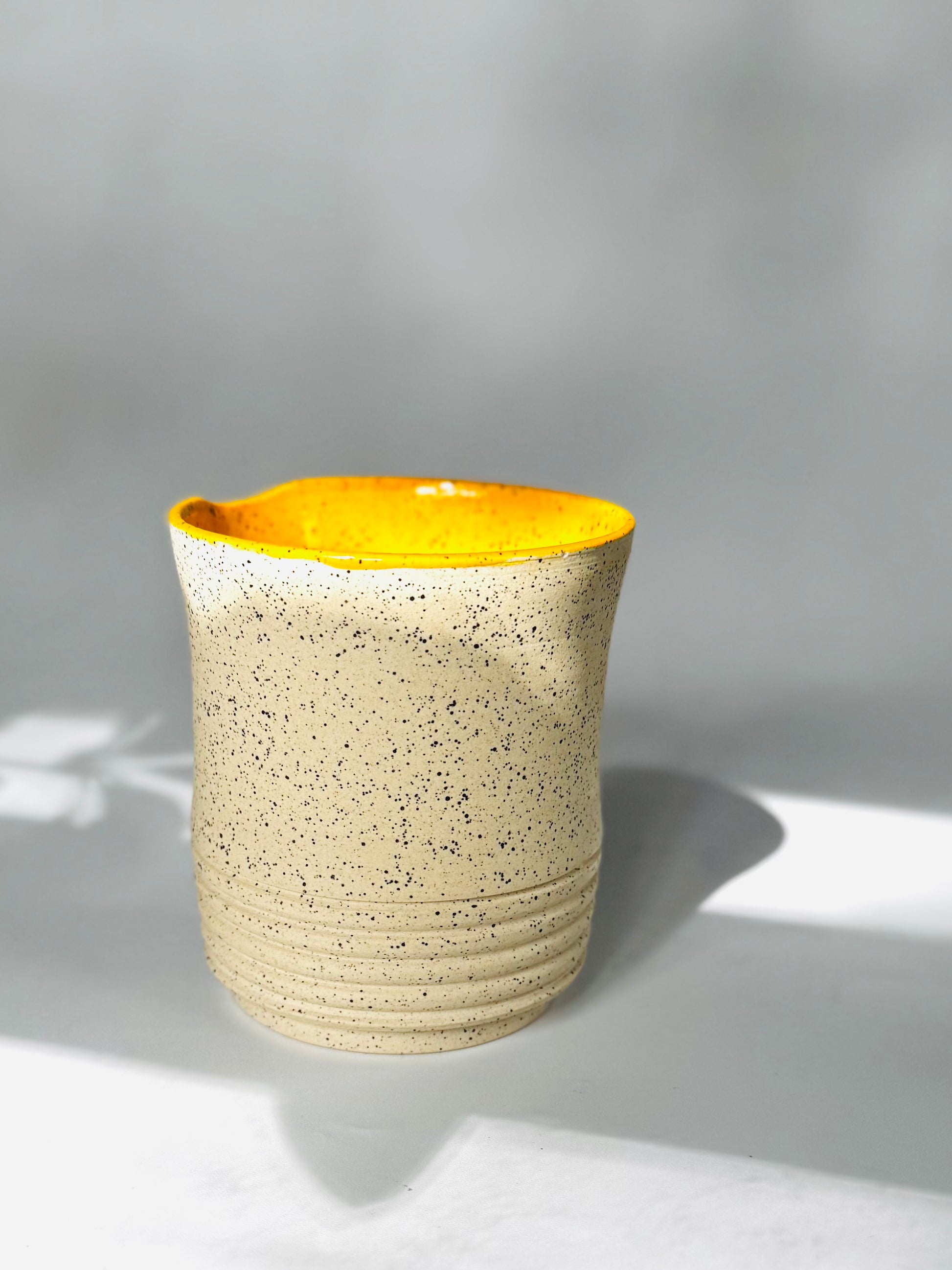 Ceramic tumbler mug with yellow interior on a black background