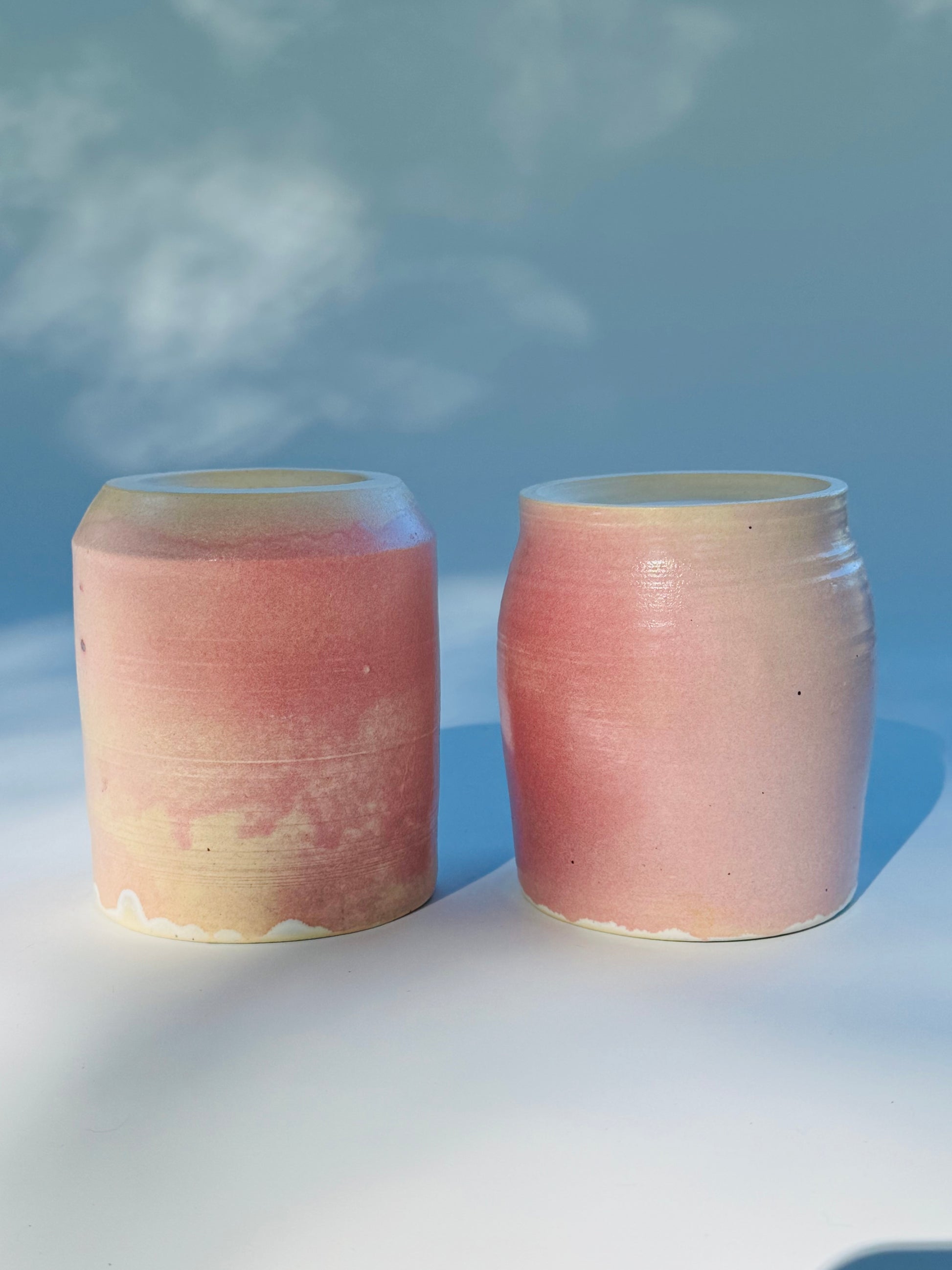 Flipped over view of two Large Kissy Cup Tumblers by Rita Strayer Ceramics of Savannah. This design features a cascading flux rim, various sea foam interior and celadon bloom shads. Stoneware, microwavable, black lip design with pink dominant colors.