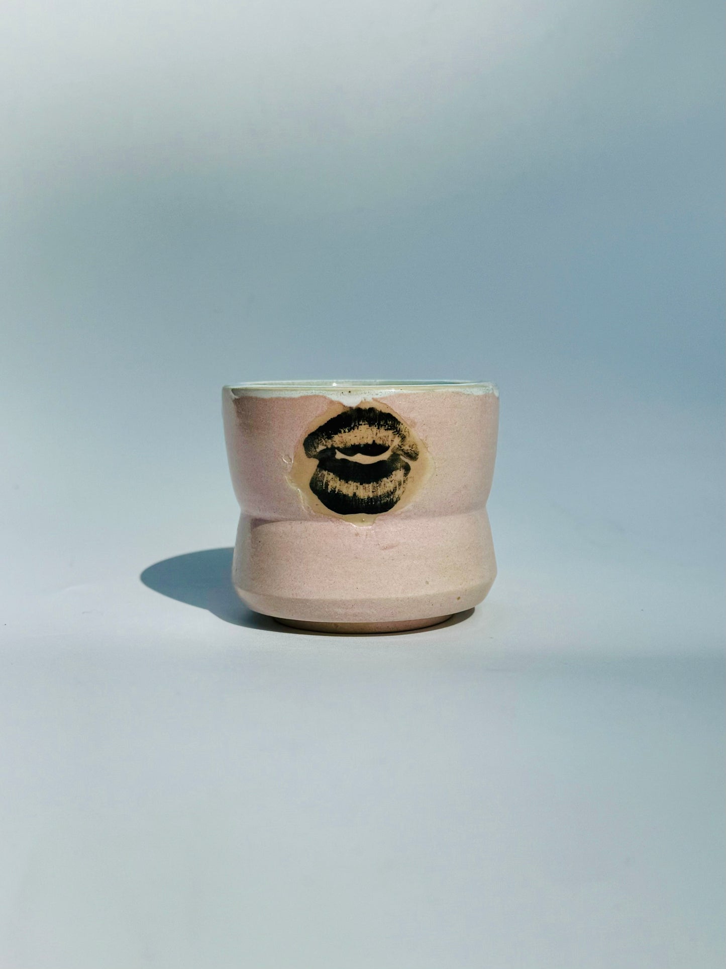 A straight ahead view of the Kissy Cup Mini-sized ceramic cup. Created by Rita Strayer Ceramics of Savannah. Features green interior and black lip design on a light grey background.