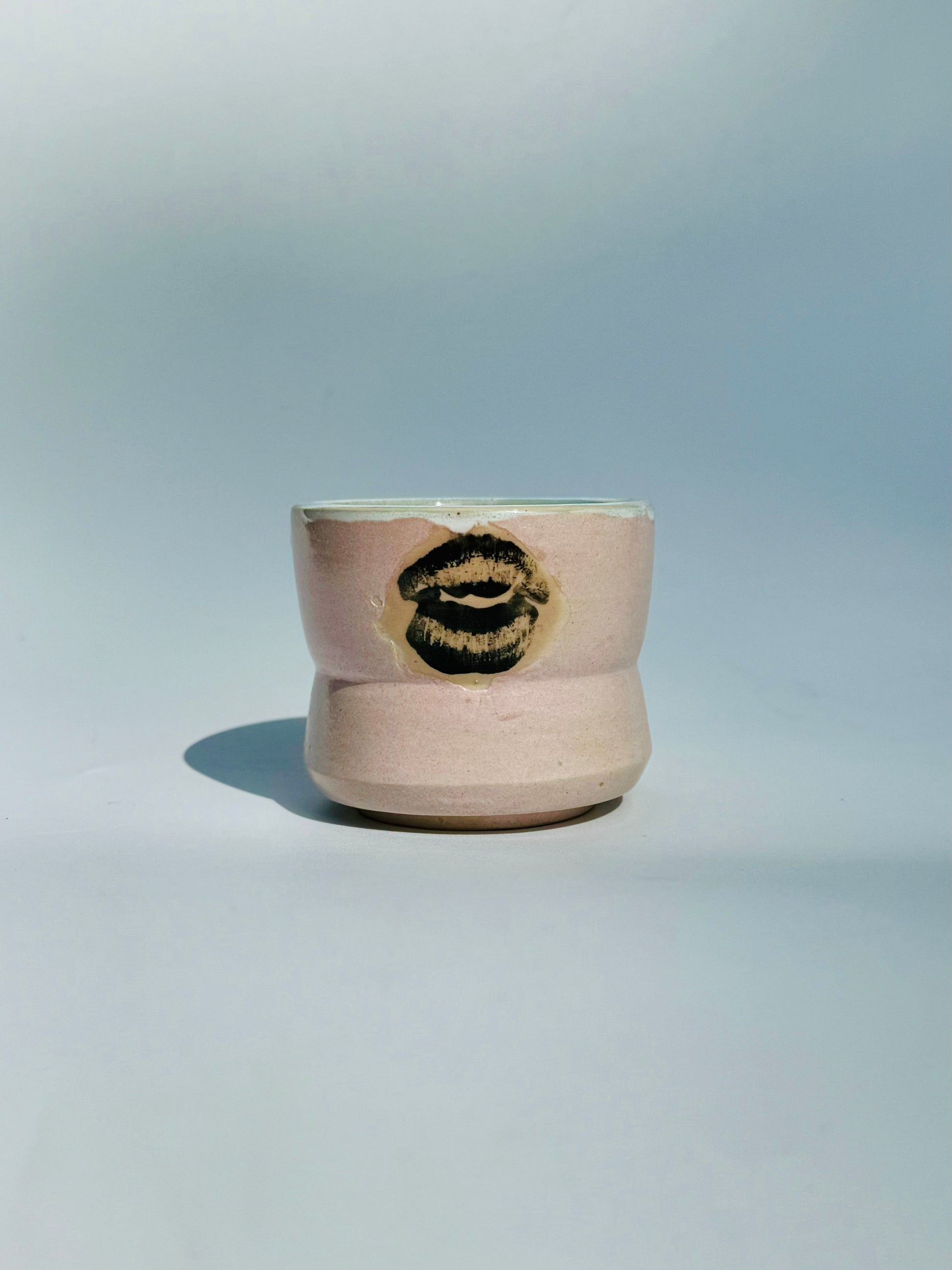 A straight ahead view of the Kissy Cup Mini-sized ceramic cup. Created by Rita Strayer Ceramics of Savannah. Features green interior and black lip design on a light grey background.