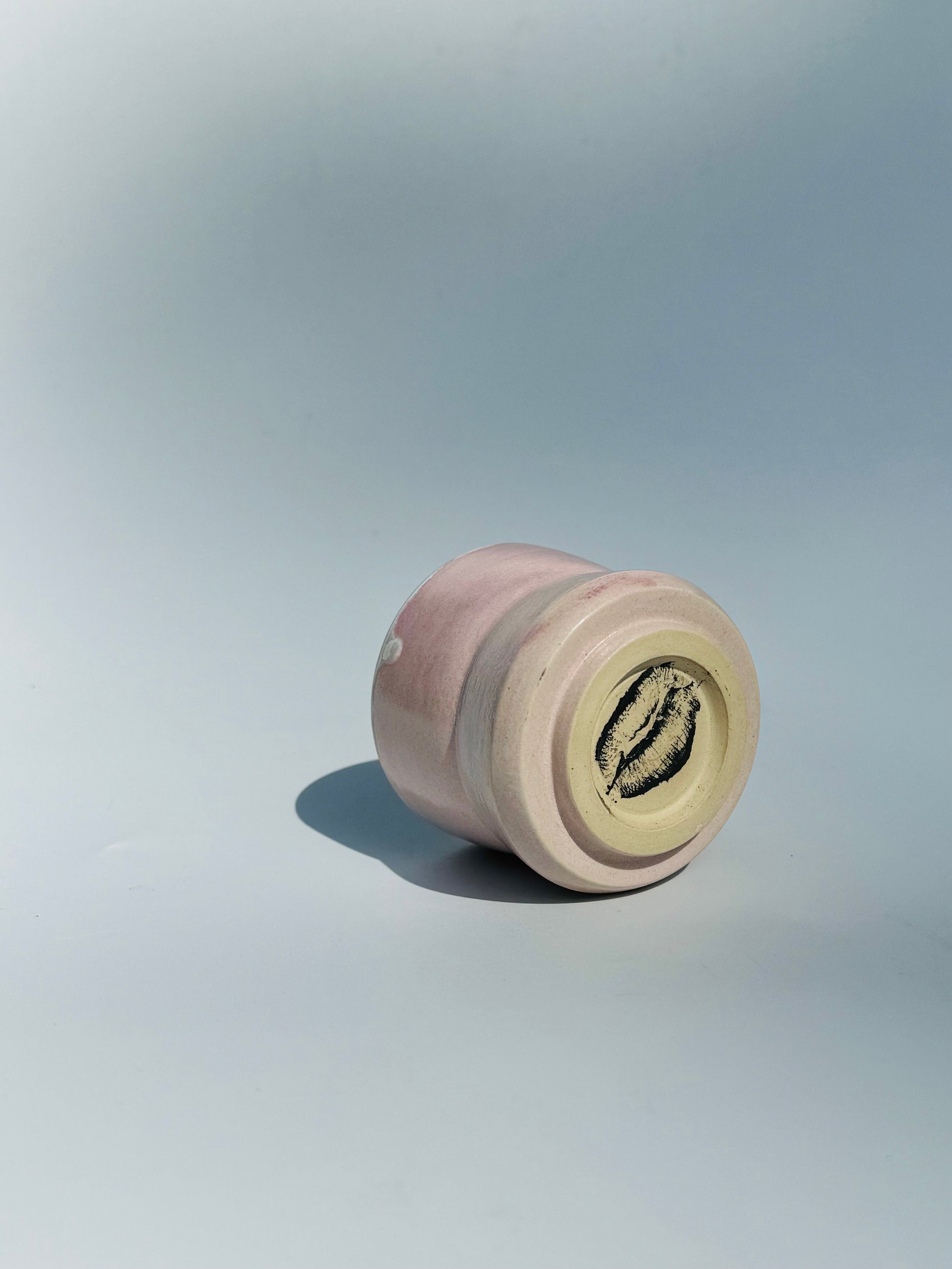 An on its side ahead view from underneath the Kissy Cup Mini-sized ceramic cup. Created by Rita Strayer Ceramics of Savannah. Features green interior and black lip design on a light grey background.