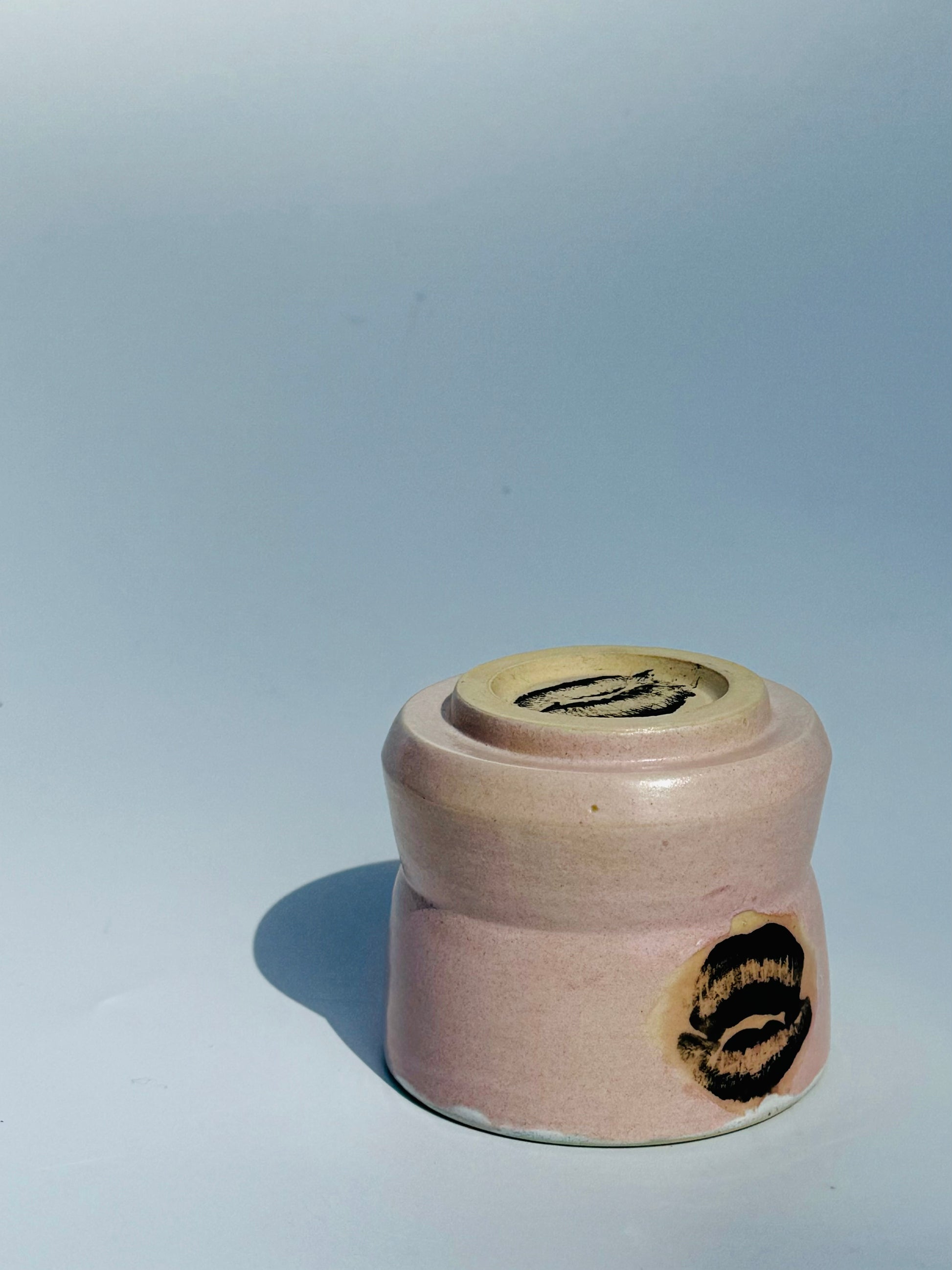 An upside down view of the Kissy Cup Mini-sized ceramic cup. Created by Rita Strayer Ceramics of Savannah. Features green interior and black lip design on a light grey background.