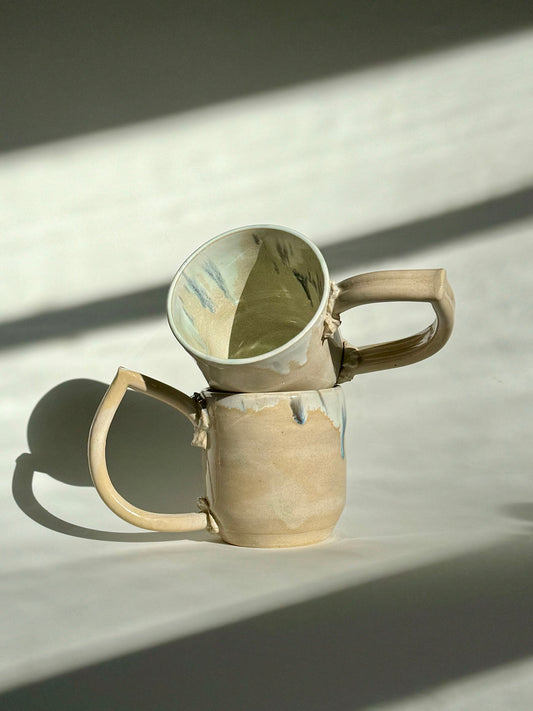 Teardrop Handle Mugs (pair) - only from Rita Strayer Ceramics of Savannah. Asymmetrical pair of mugs with a roomy handle hold. 8 oz Teardrop Handle Mugs via potters wheel, carved, & hand-built. Glazes dipped, sprayed, & hand-painted. View of two stacked mugs.