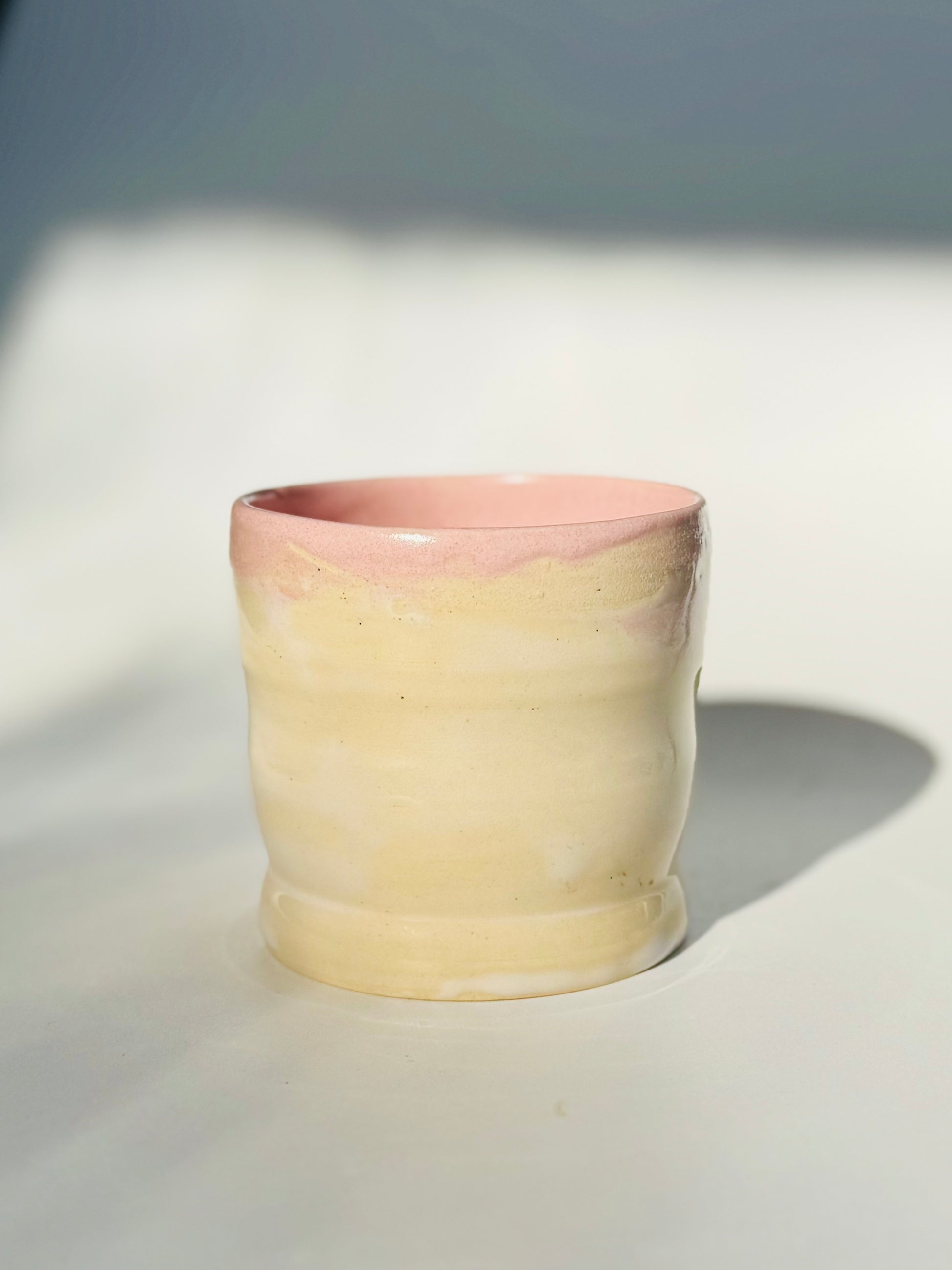 Closer view of the Little Milk Cup tumbler design by Rita Strayer Ceramics of Savannah, GA. A tumbler with convenient finger grooves to accommodate little hands, sleepy hands, and slippery hands too. Two-tone pink interior, beige exterior colouring.
