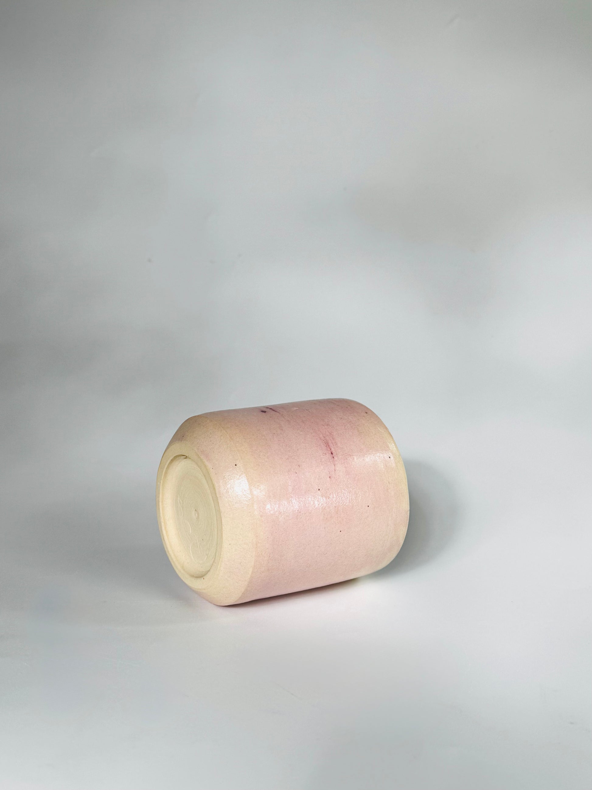 Sideways turned over view of the Small Kissy Cup Tumbler by Rita Strayer Ceramics of Savannah. This design features a cascading flux rim, various sea foam interior and celadon bloom shads. Stoneware, microwavable, black lip design with pink dominant colors.