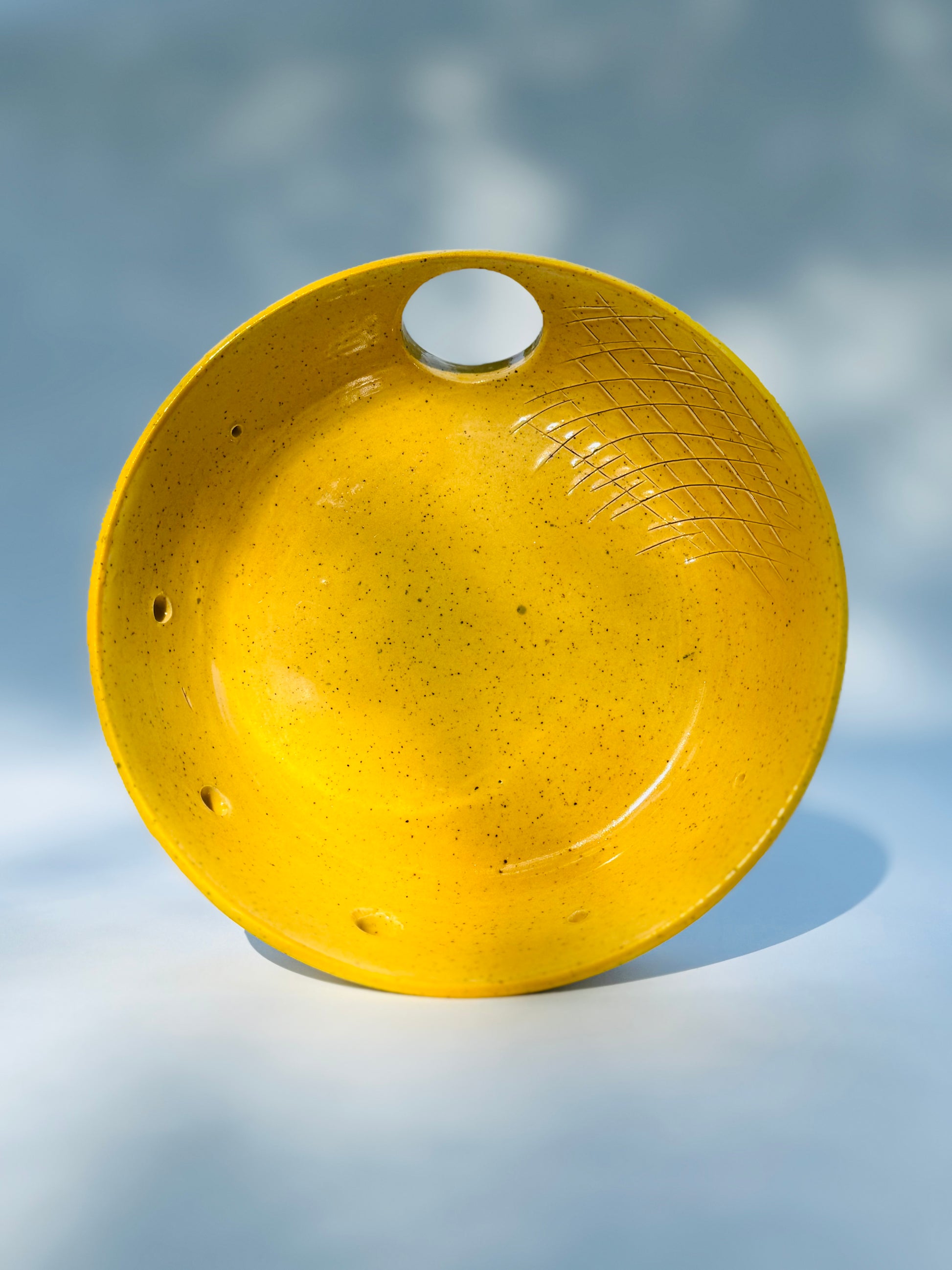 Lifted up view of the One thumb hole herb stripper with garlic grater design in yellow from Rita Strayer Ceramics of Savannah. Easily strip leaves from your favorite herbs. Stoneware clay with celadon glaze. Thumb hole to allow for easier handling while stripping.