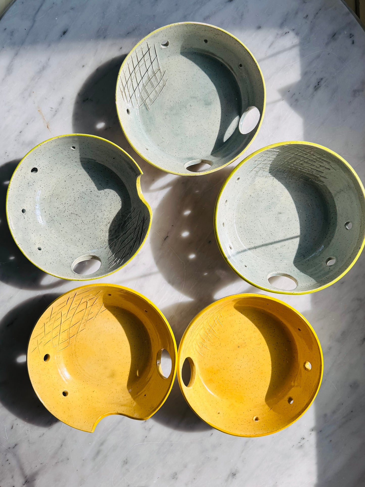 Spread out overhead view of five different Herb stripper with Garlic Grater designs by Rita Strayer Ceramics of Savannah. Easily strip leaves from your favorite herb. Made from Stoneware clay. Available in chartreuse (green) or yellow interior bowl colors, and with either 1 or 2 thumb holes to easily control when you're using it, or hang up when you're done.