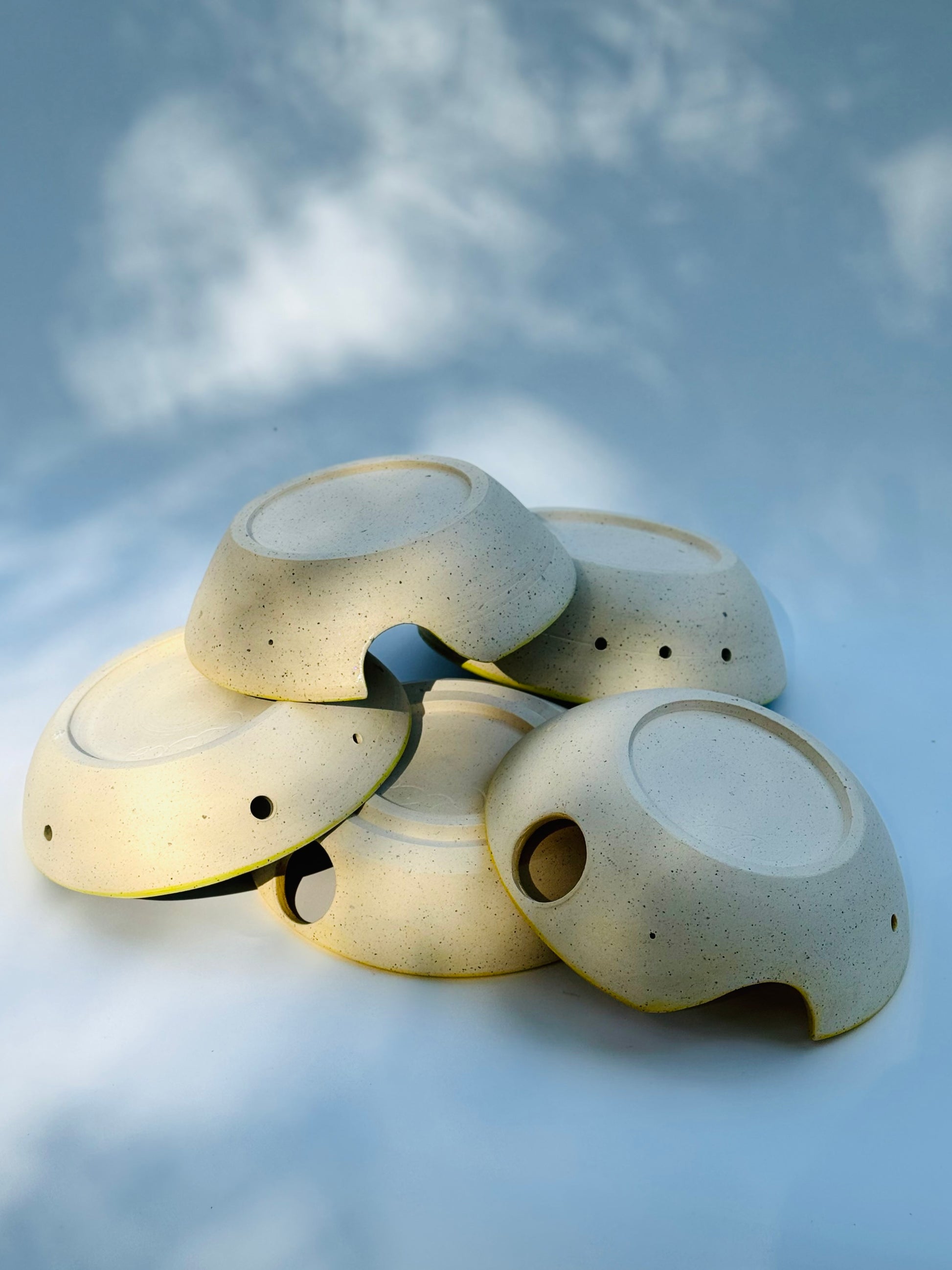 Stacked upside down view of five different Herb stripper with Garlic Grater designs by Rita Strayer Ceramics of Savannah. Easily strip leaves from your favorite herb. Made from Stoneware clay. Available in interior bowl colors of chartreuse (green) or yellow. Some come with 1 or 2 thumb holes -- each version gives you control when you use it, and storage options when you put it away.