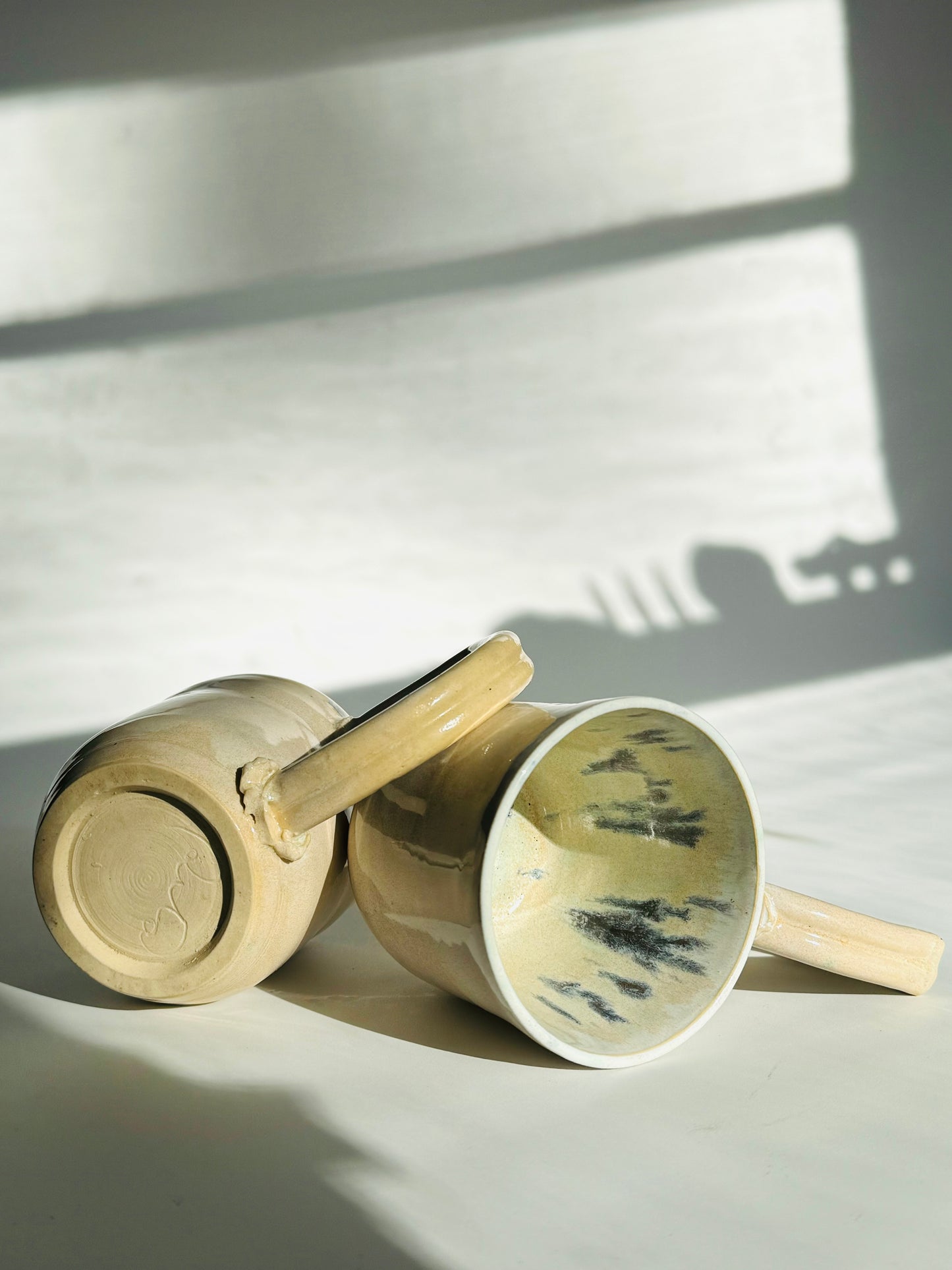 Teardrop Handle Mugs (pair) - only from Rita Strayer Ceramics of Savannah. Side by side on their side view. Asymmetrical pair of mugs with a roomy handle hold. 8 oz Teardrop Handle Mugs via potters wheel, carved, & hand-built. Glazes dipped, sprayed, & hand-painted.