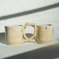Teardrop Handle Mugs (pair) - only from Rita Strayer Ceramics of Savannah. Side view, handle overlapping handle. Asymmetrical pair of mugs with a roomy handle hold. 8 oz Teardrop Handle Mugs via potters wheel, carved, & hand-built. Glazes dipped, sprayed, & hand-painted.