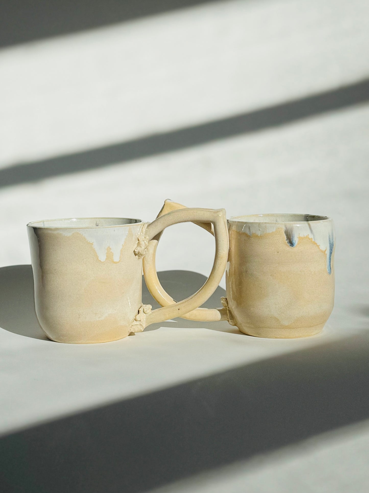 Teardrop Handle Mugs (pair) - only from Rita Strayer Ceramics of Savannah. Side view, handle overlapping handle. Asymmetrical pair of mugs with a roomy handle hold. 8 oz Teardrop Handle Mugs via potters wheel, carved, & hand-built. Glazes dipped, sprayed, & hand-painted.