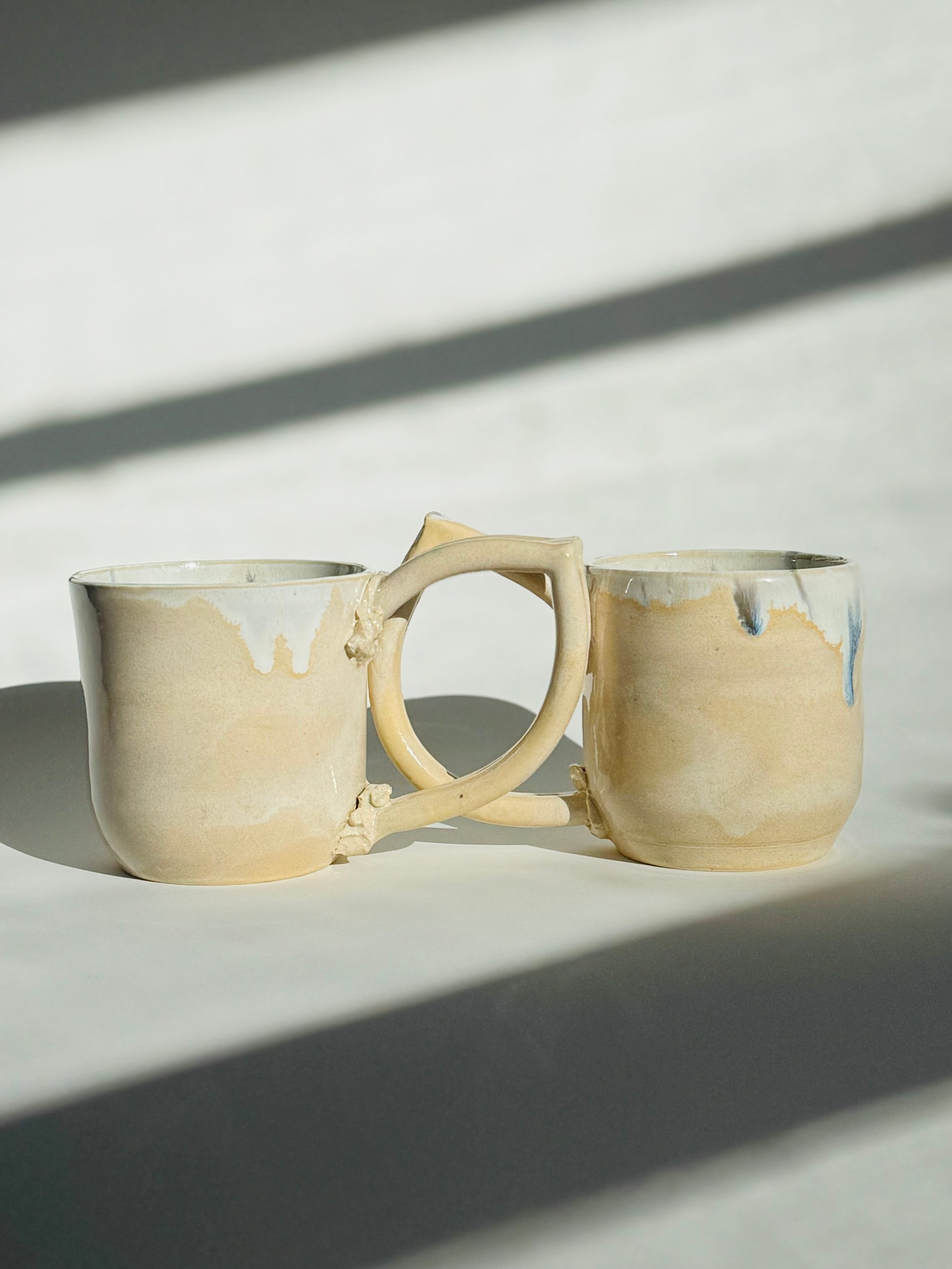 Teardrop Handle Mugs (pair) - only from Rita Strayer Ceramics of Savannah. Side view, handle overlapping handle. Asymmetrical pair of mugs with a roomy handle hold. 8 oz Teardrop Handle Mugs via potters wheel, carved, & hand-built. Glazes dipped, sprayed, & hand-painted.