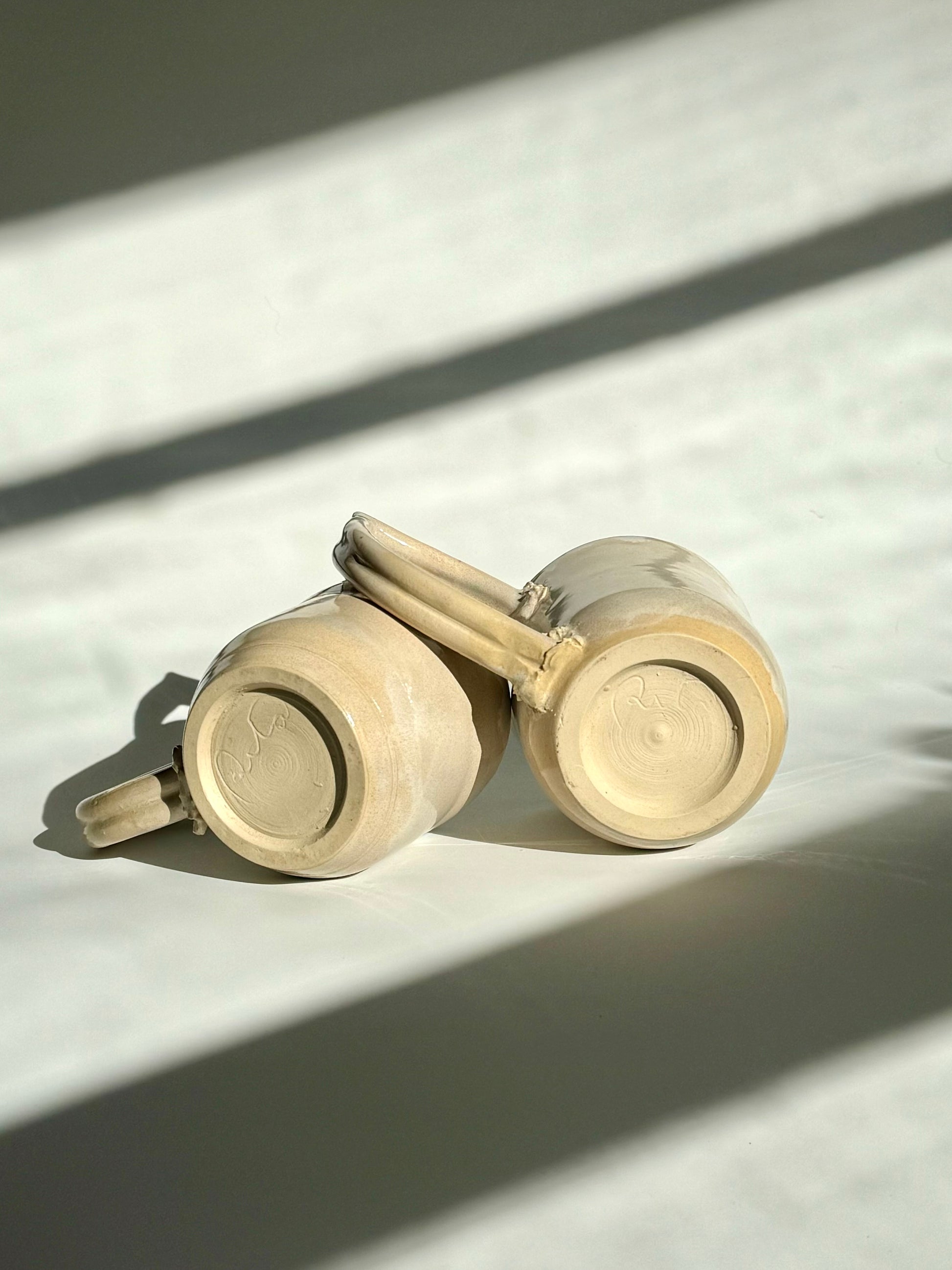 Teardrop Handle Mugs (pair) - only from Rita Strayer Ceramics of Savannah - bottom up view of mugs on their side. Asymmetrical pair of mugs with a roomy handle hold. 8 oz Teardrop Handle Mugs via potters wheel, carved, & hand-built. Glazes dipped, sprayed, & hand-painted.