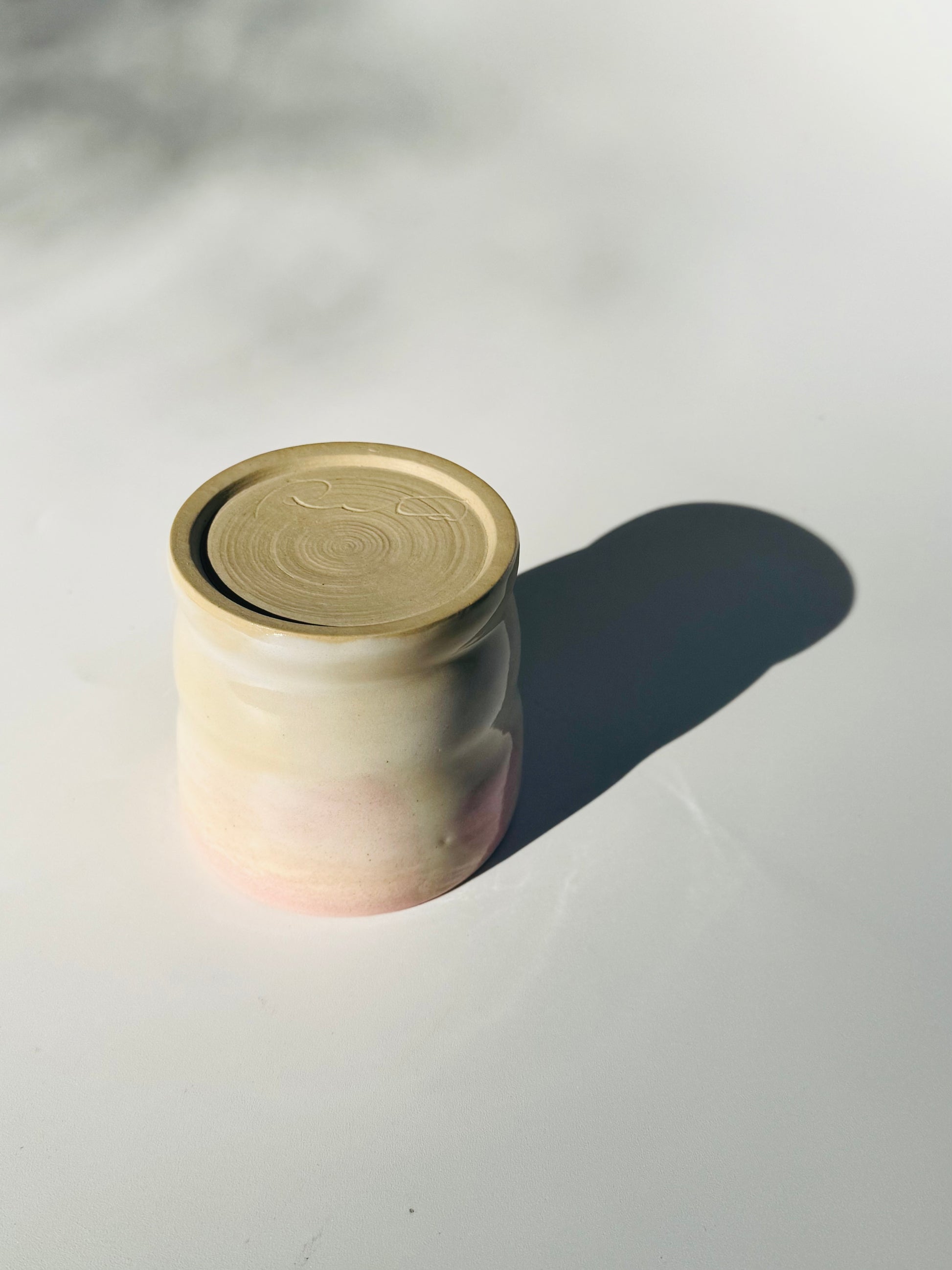 Upside down overhead view of the Little Milk Cup tumbler design by Rita Strayer Ceramics of Savannah, GA. A tumbler with convenient finger grooves to accommodate little hands, sleepy hands, and slippery hands too. Two-tone pink and beige colouring.